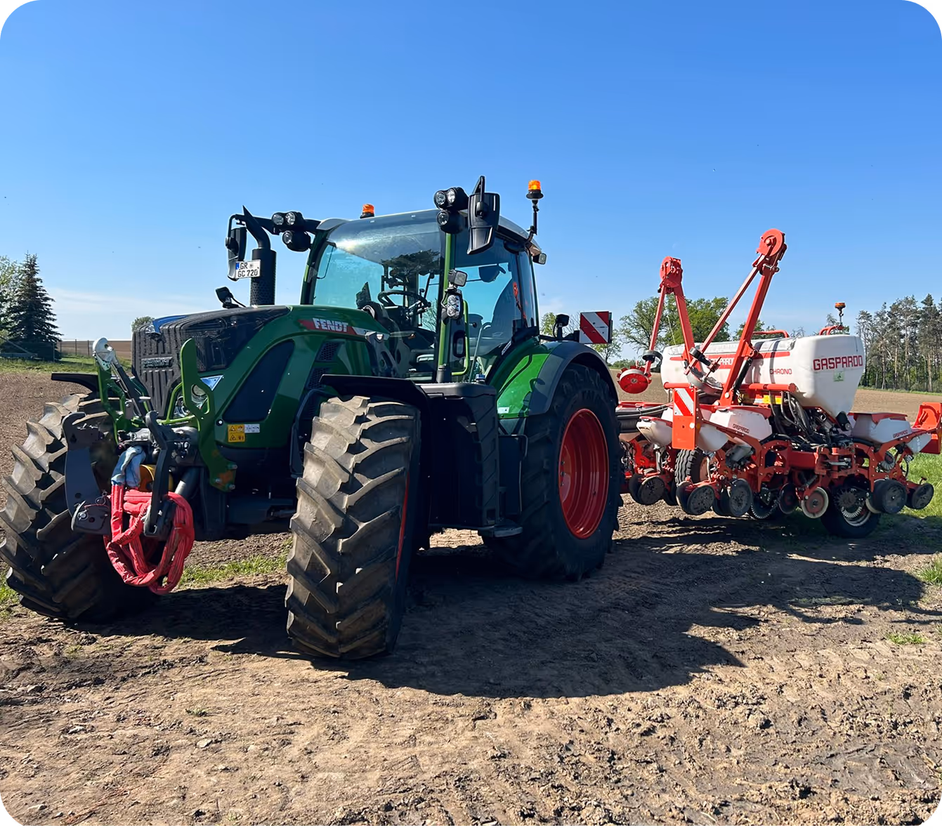 Grüner Fendt-Traktor mit rotem Anbaugerät für die Feldarbeit auf einem Acker unter blauem Himmel.
