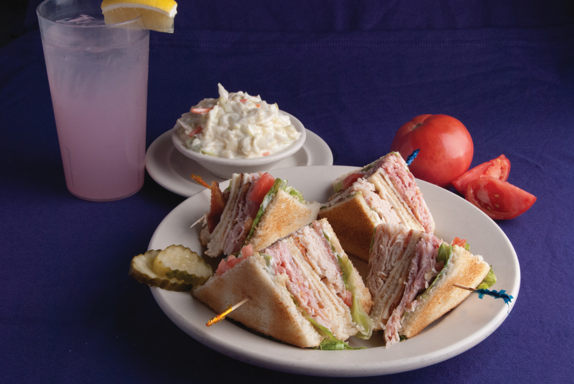 Crispy chicken sandwich with bacon, melted cheddar cheese, lettuce, tomato, and mayonnaise on a bun served with French fries on a white plate.