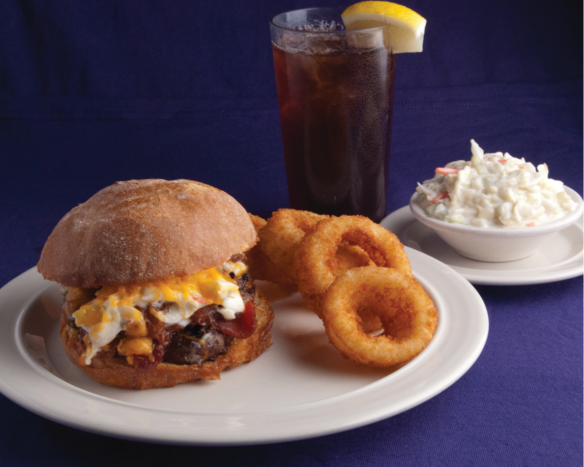 Crispy fried chicken sandwich with pickles and mayonnaise on a bun served with a side of French fries on a white plate.