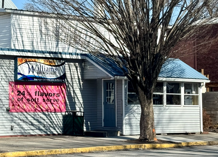 Outdoor seating area with black metal tables and chairs under blue and beige umbrellas outside a blue and white sandwich shop.