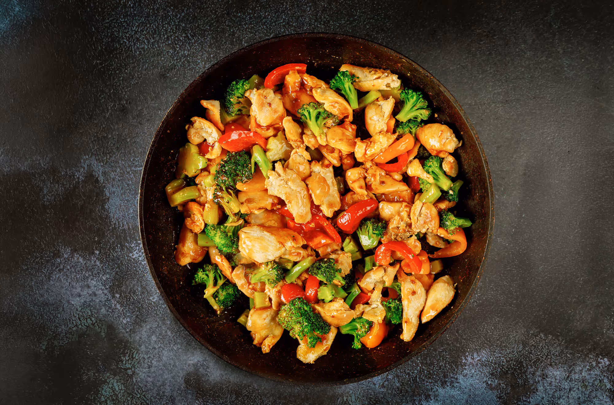 Stir-fry dish with chicken, broccoli, red bell peppers, and celery in a dark pan.