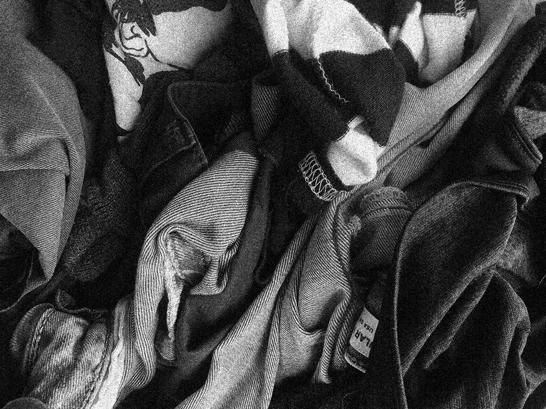 Close-up of a pile of mixed fabric clothes, showing texture and stitching details in black and white.
