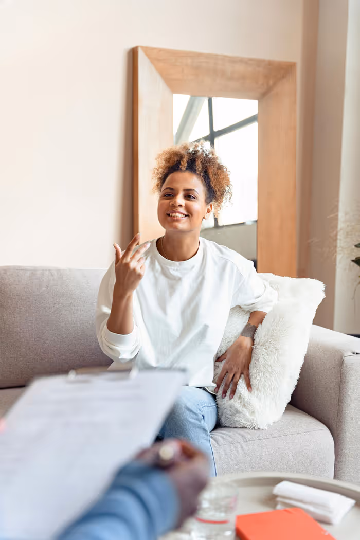 A woman smiles and speaks openly while seated comfortably on a couch during a therapy session.