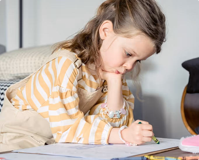 A young girl sits quietly and focuses intently on drawing in a notebook, illustrating a child's concentration and inner world.