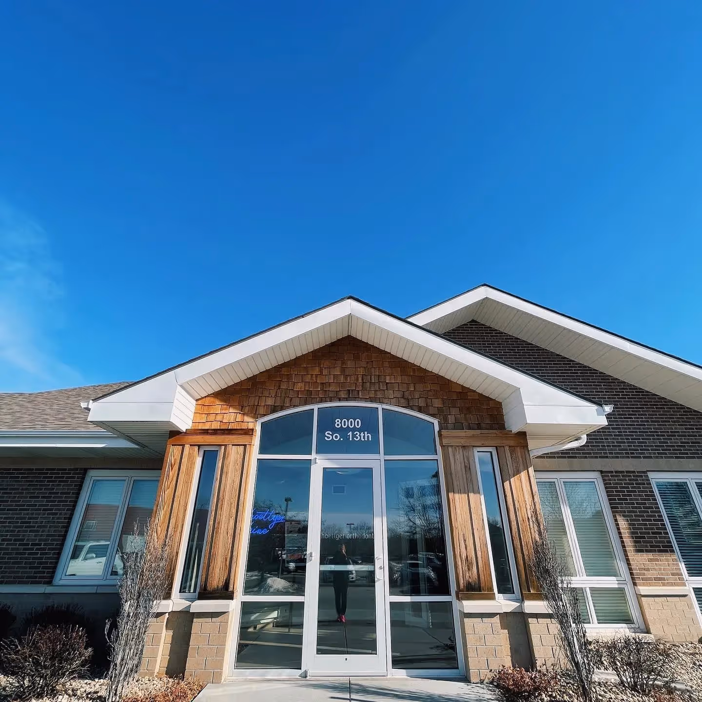 Modern brick and wood office building entrance with glass door under a clear blue sky.