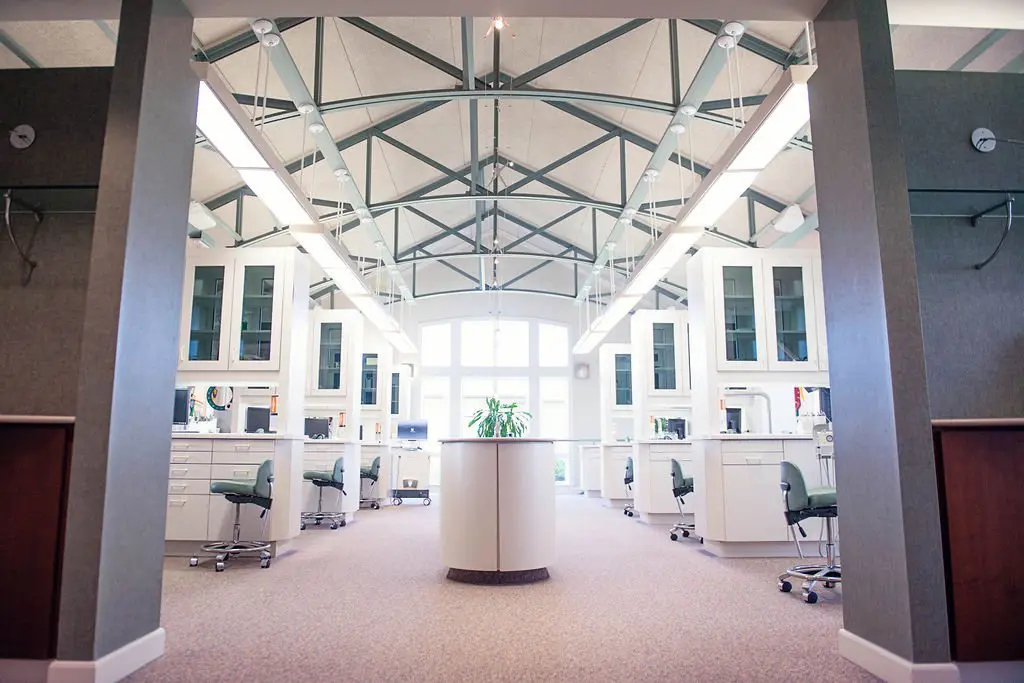 Bright, spacious dental or medical office with white cabinetry, green rolling chairs, and exposed beam ceiling.