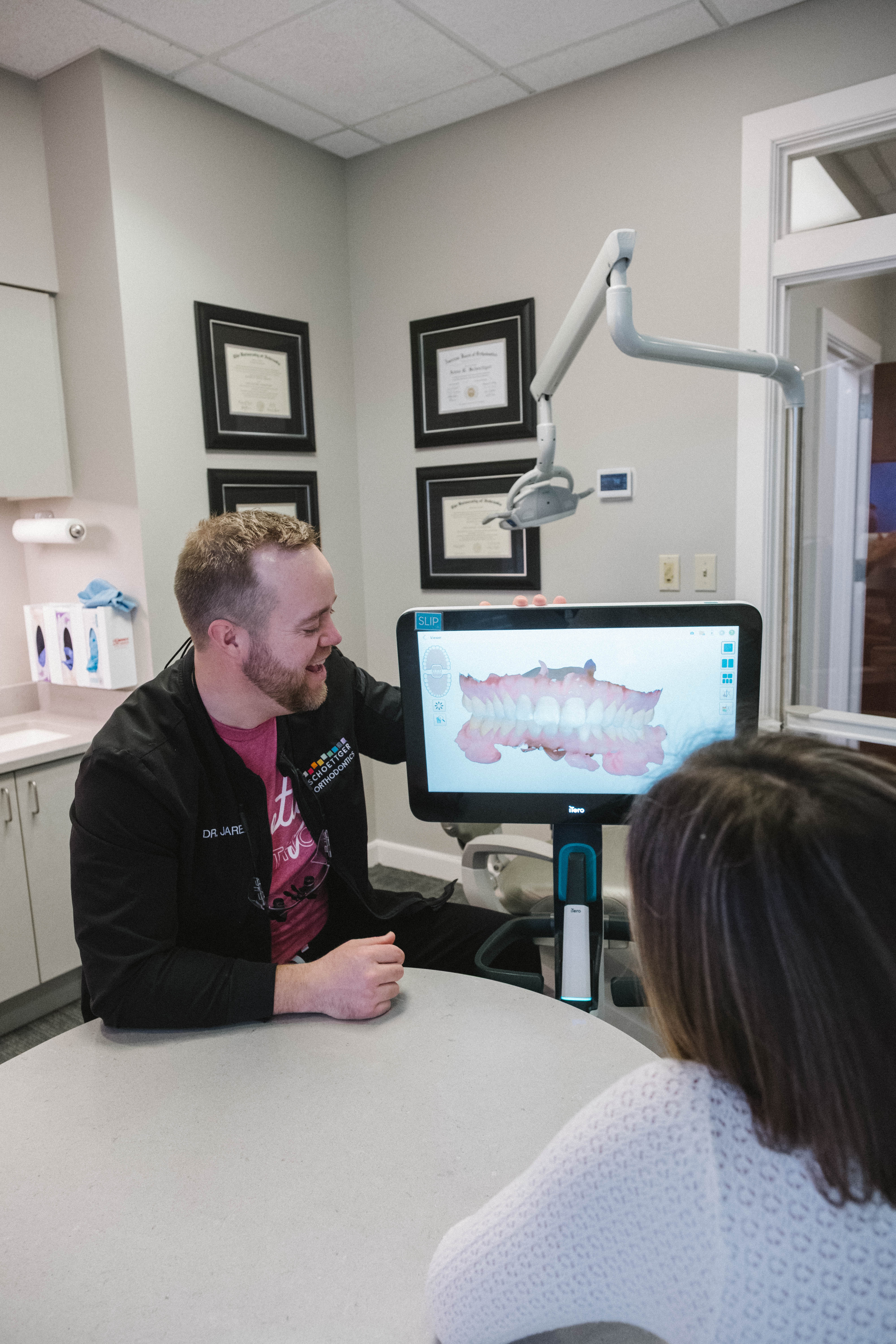 Orthodontist shows patient a 3D digital scan of teeth on a monitor in a consultation room.