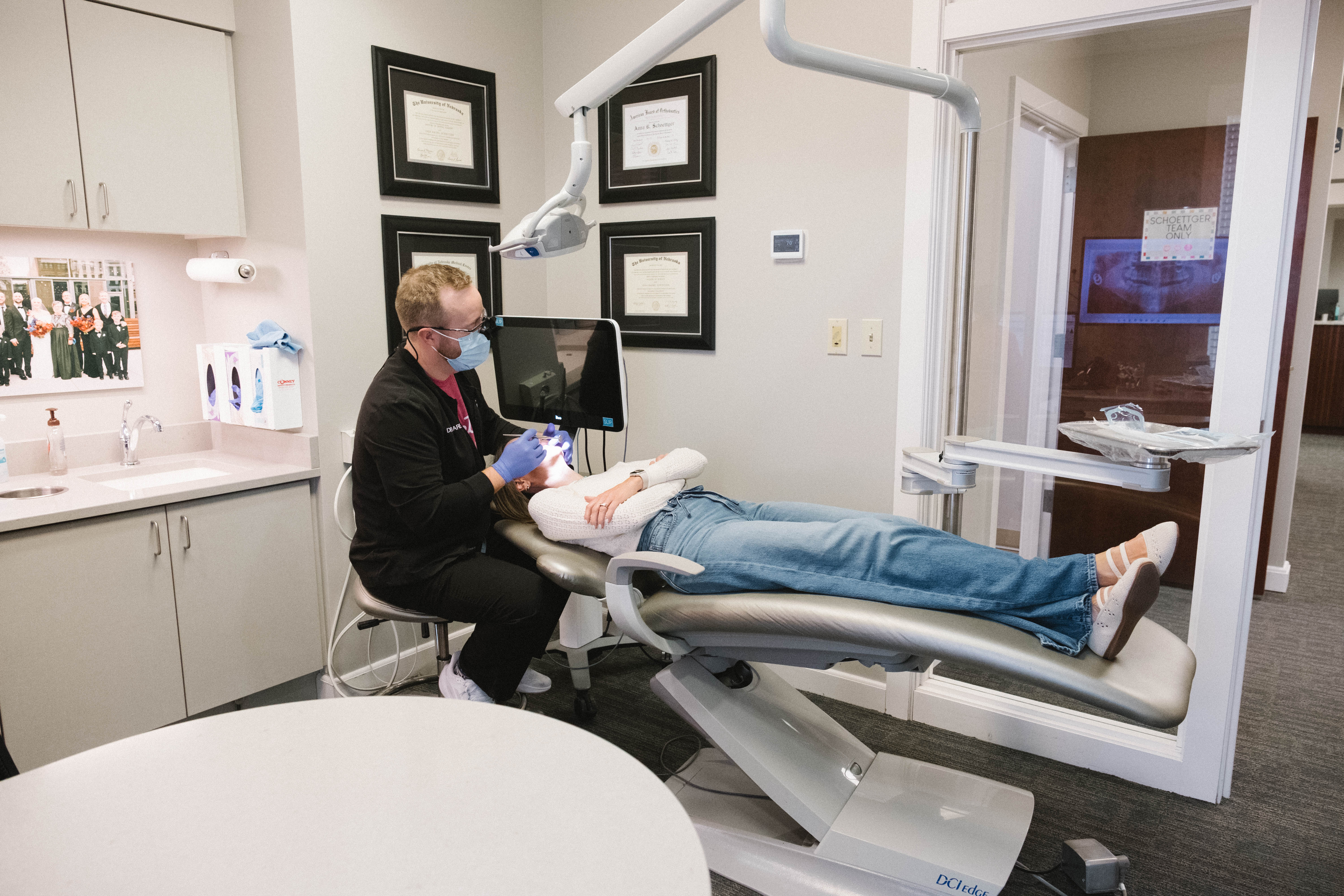 Dentist wearing mask and gloves examines woman lying on dental chair in a clinic room.