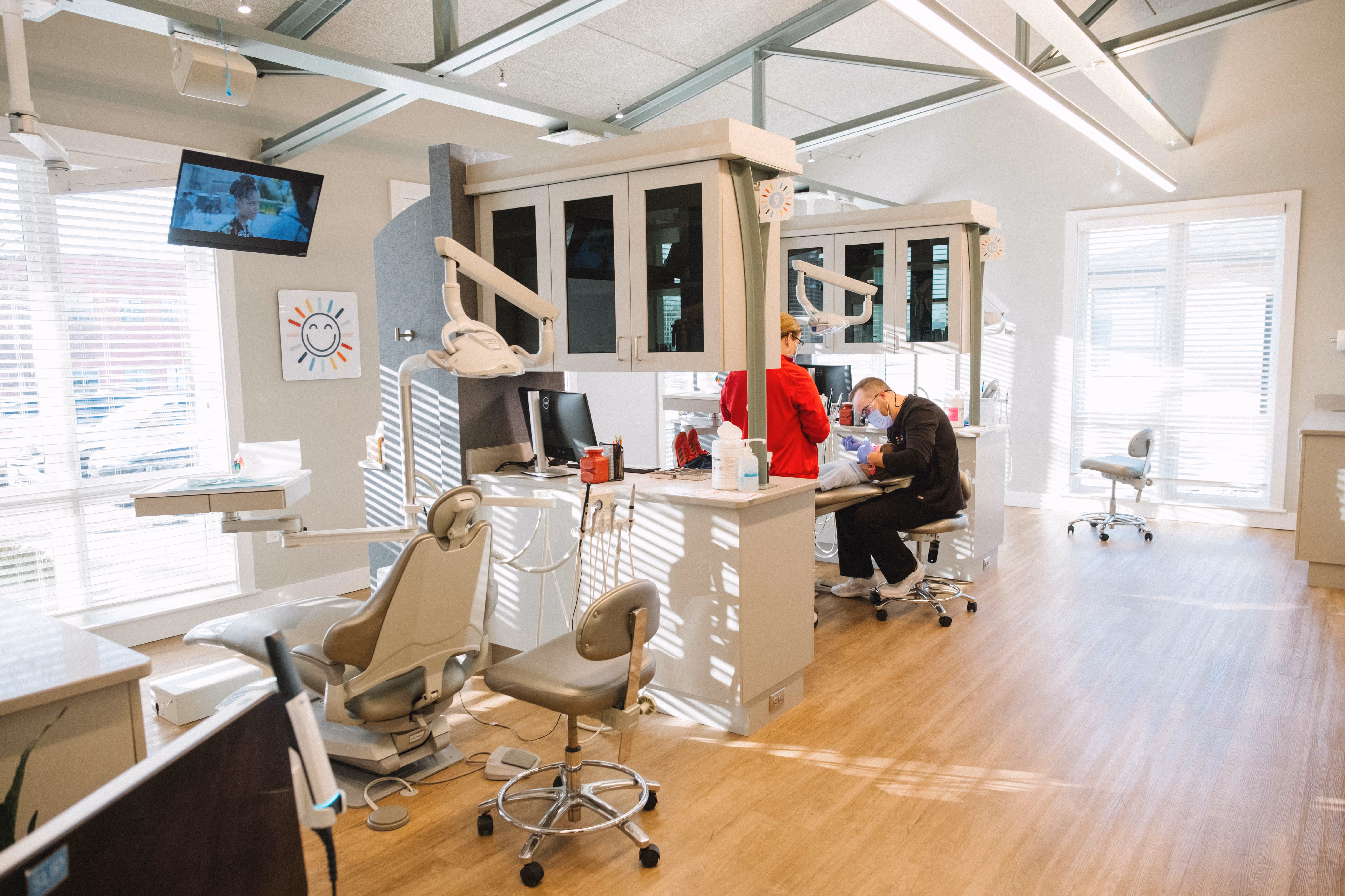 Modern bright dental clinic with two dental chairs and a dentist working on a patient.