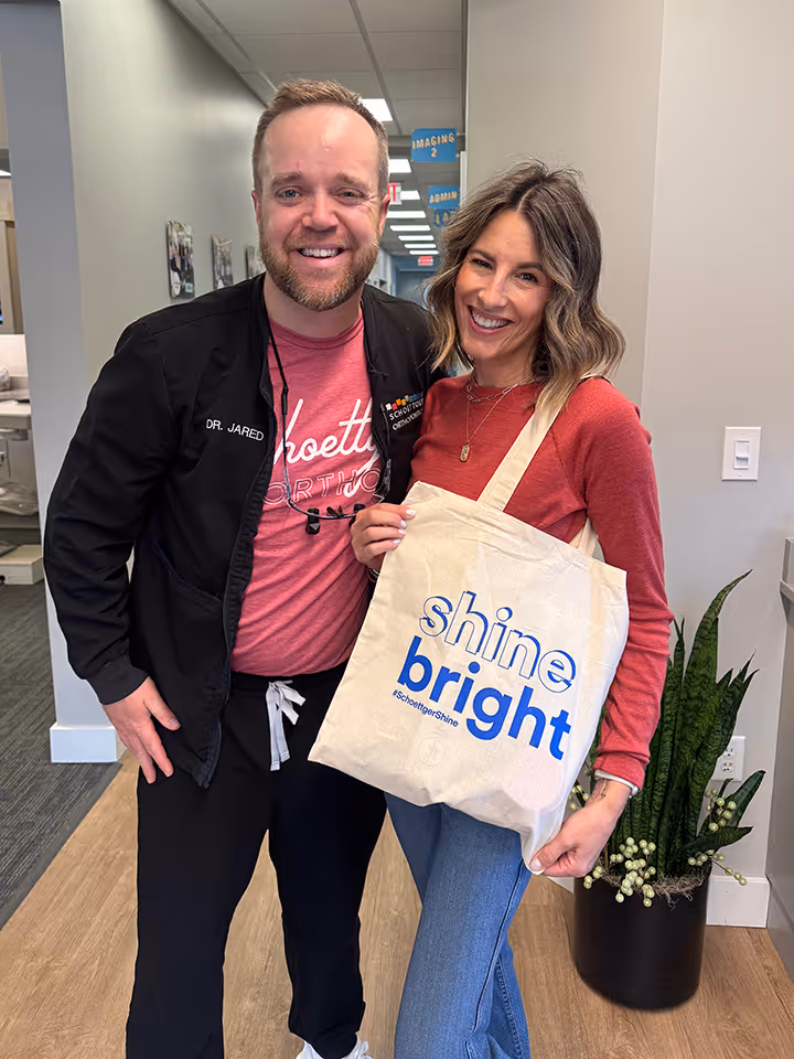Smiling man wearing black jacket and woman holding tote bag with Shine Bright printed in blue.