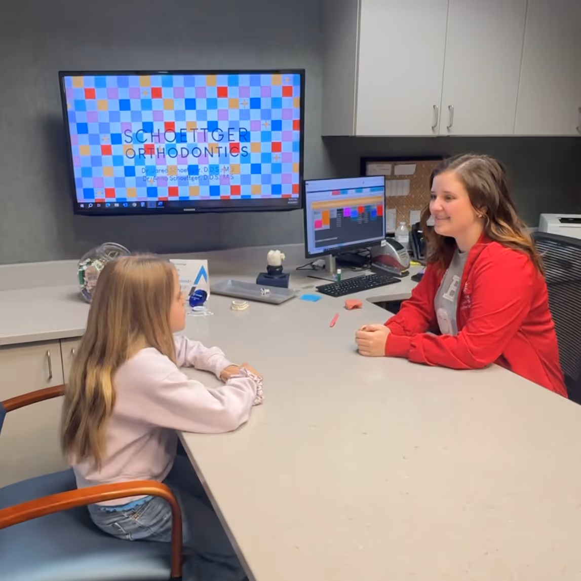 Child sitting across desk from smiling orthodontic receptionist in office at Schoettger Orthodontics.