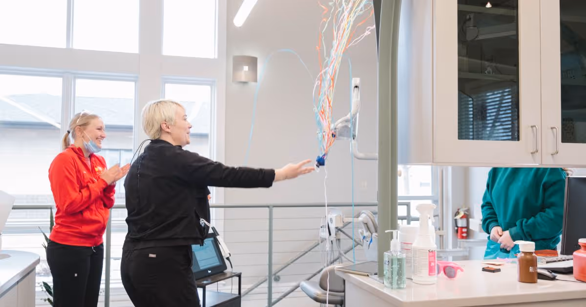 Two women smiling and clapping in a bright, modern dental office near large windows.