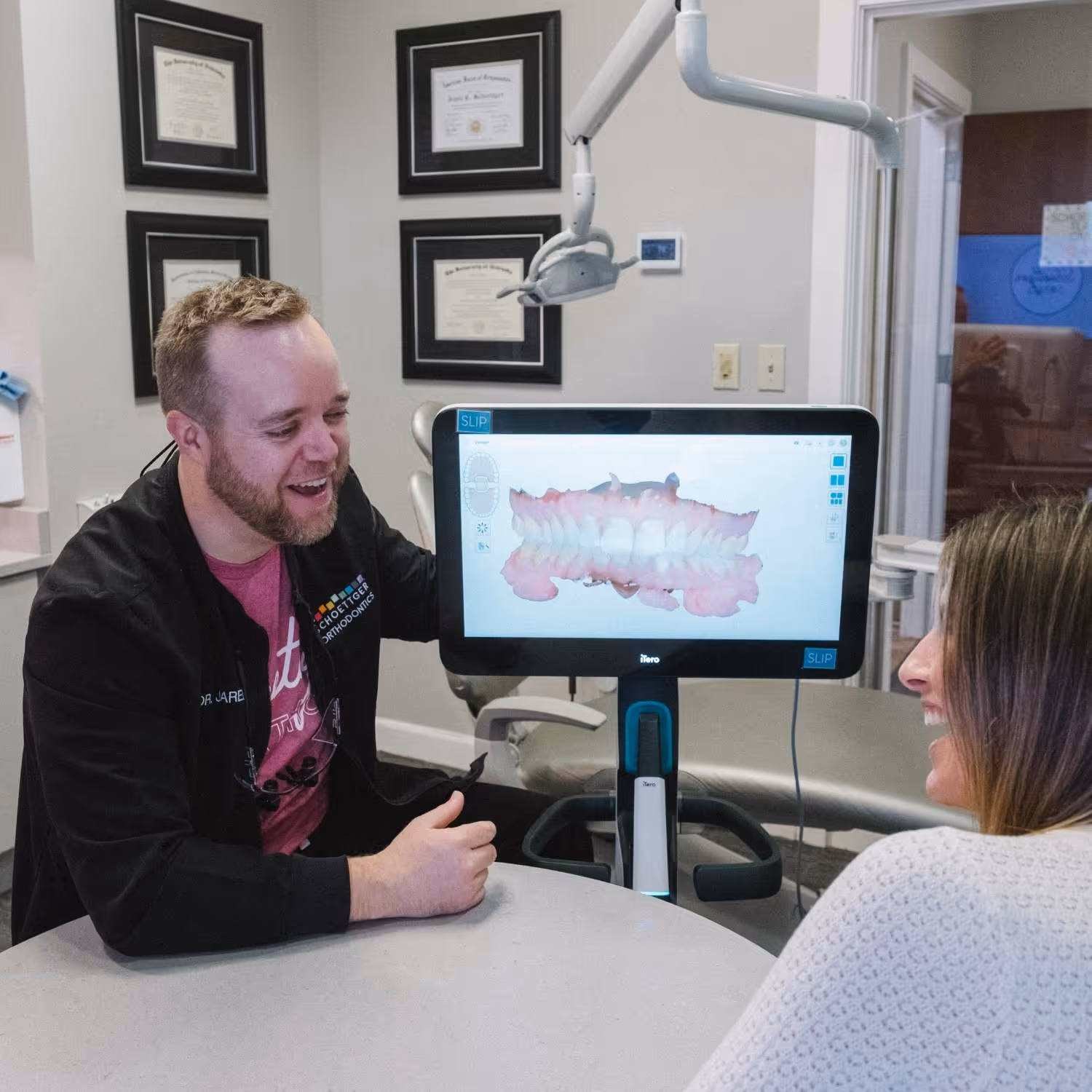 Orthodontist explaining 3D teeth scan on monitor to female patient at dental office.