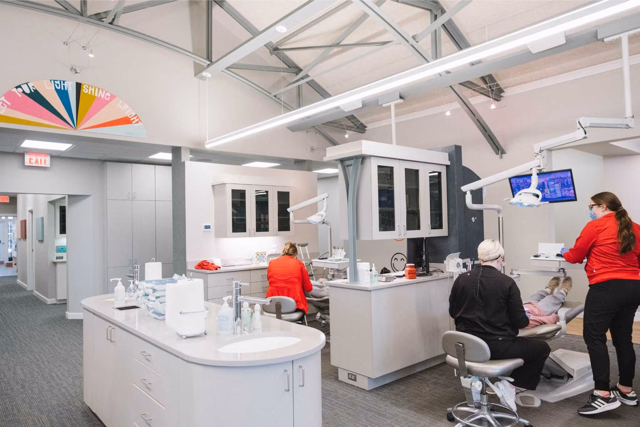 Dental clinic with two patients receiving care from staff in red uniforms wearing masks.