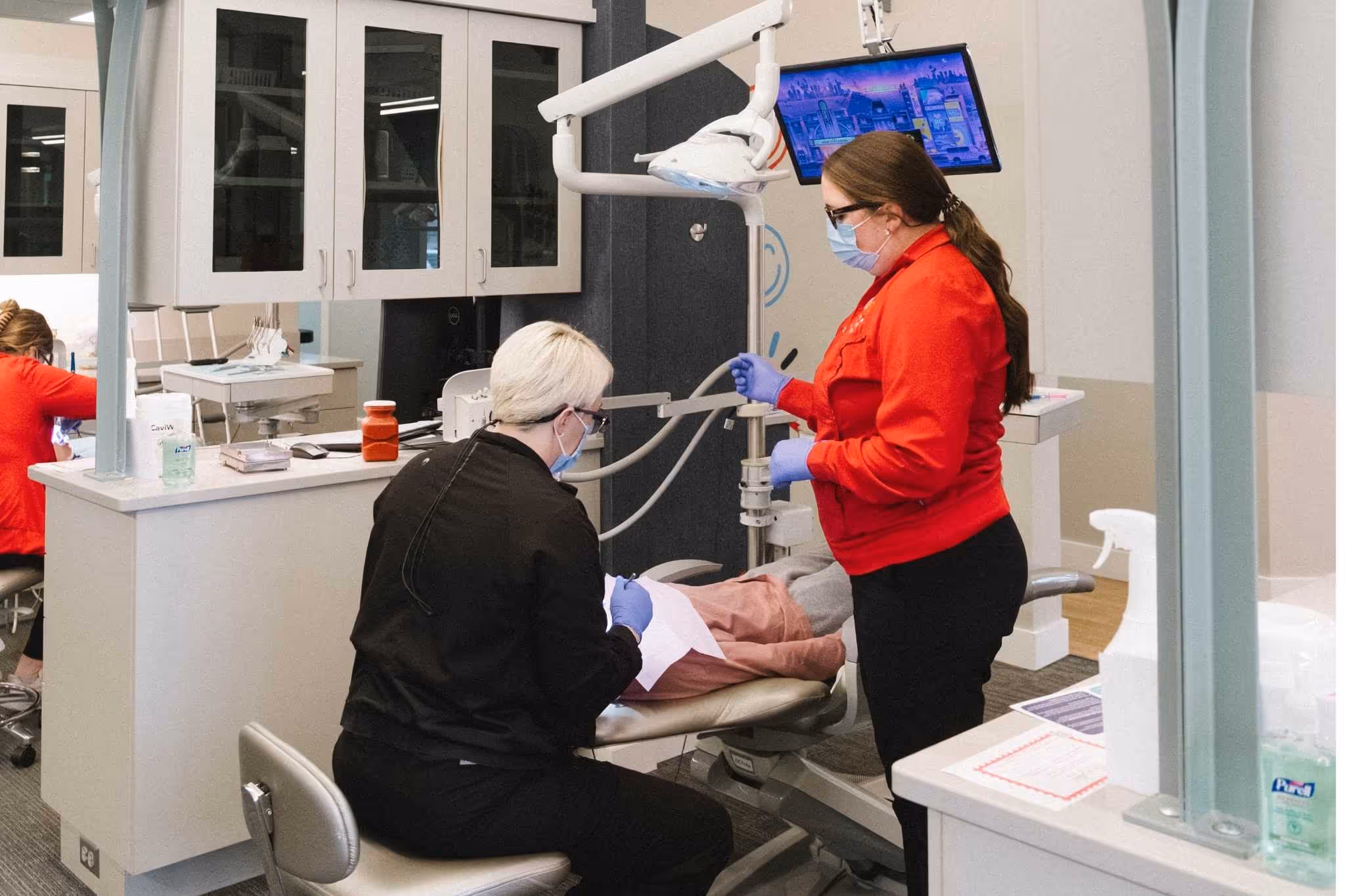 Dental professionals wearing masks and gloves treating a patient reclining in a dental chair.