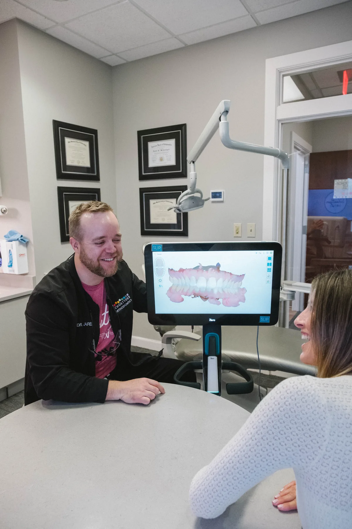 Orthodontist smiling with a patient while reviewing a digital 3D teeth scan on a monitor at Schoettger Orthodontics.