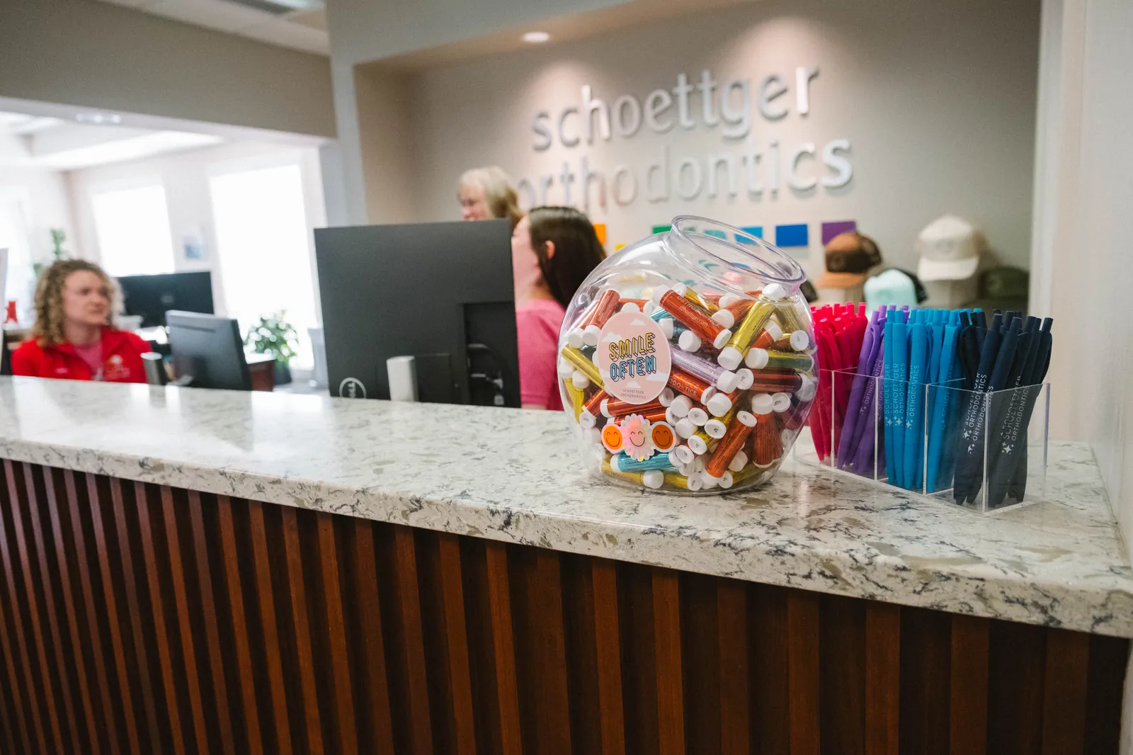 Reception desk with a container of colorful lip balms and pens at Schoettger Orthodontics office.