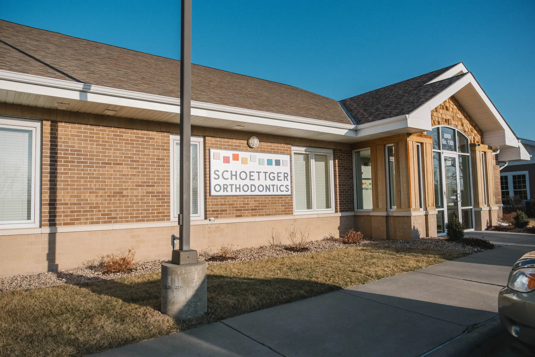 Brick building exterior with Schoettger Orthodontics sign and an entrance door under clear blue sky.