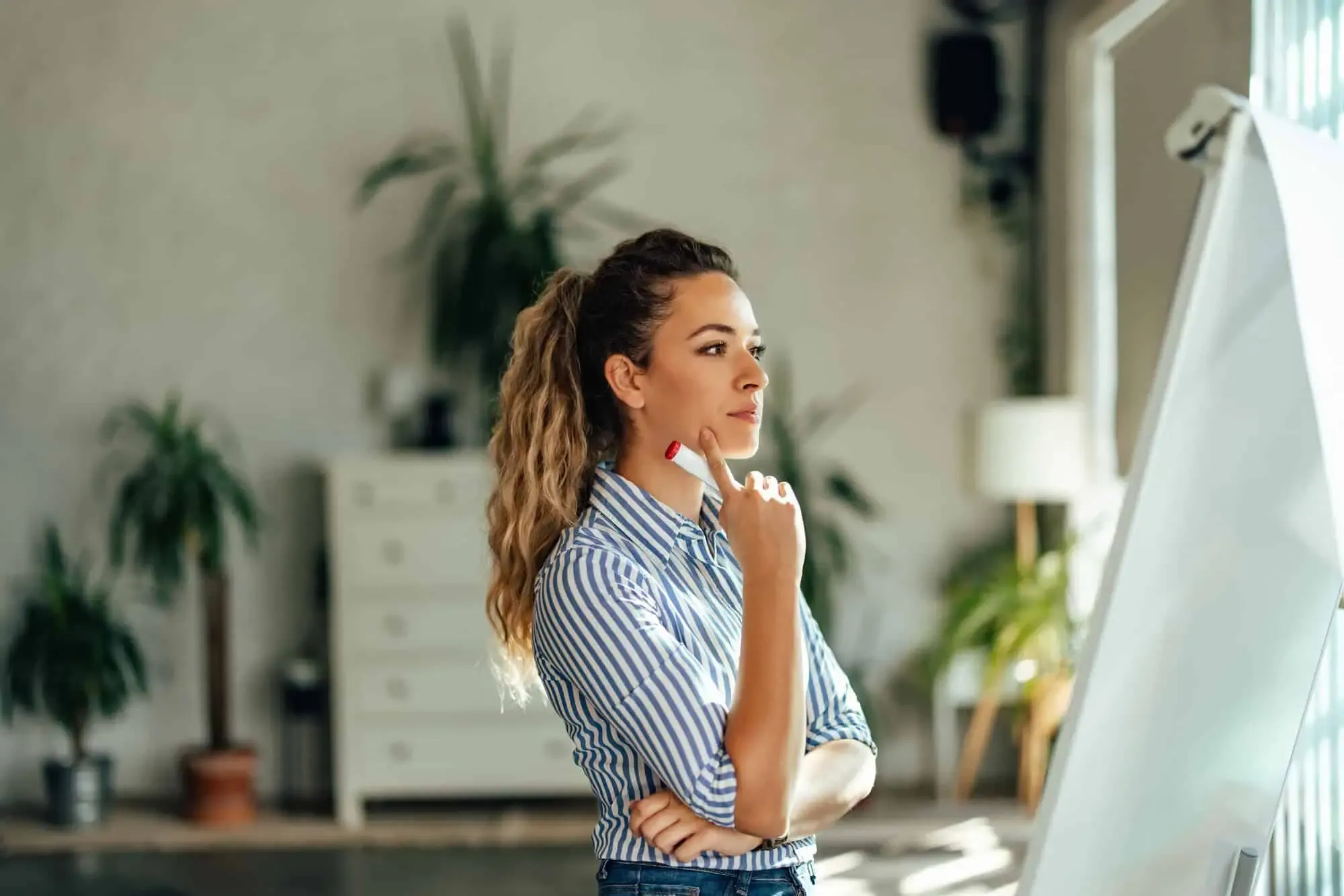 Woman holding a marker and thinking in a bright office setting.
