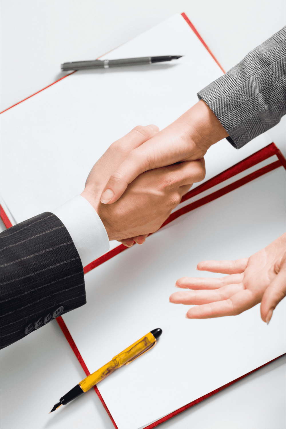 Zwei Personen geben sich vor einem geöffneten Buch mit einem Stift die Hand.