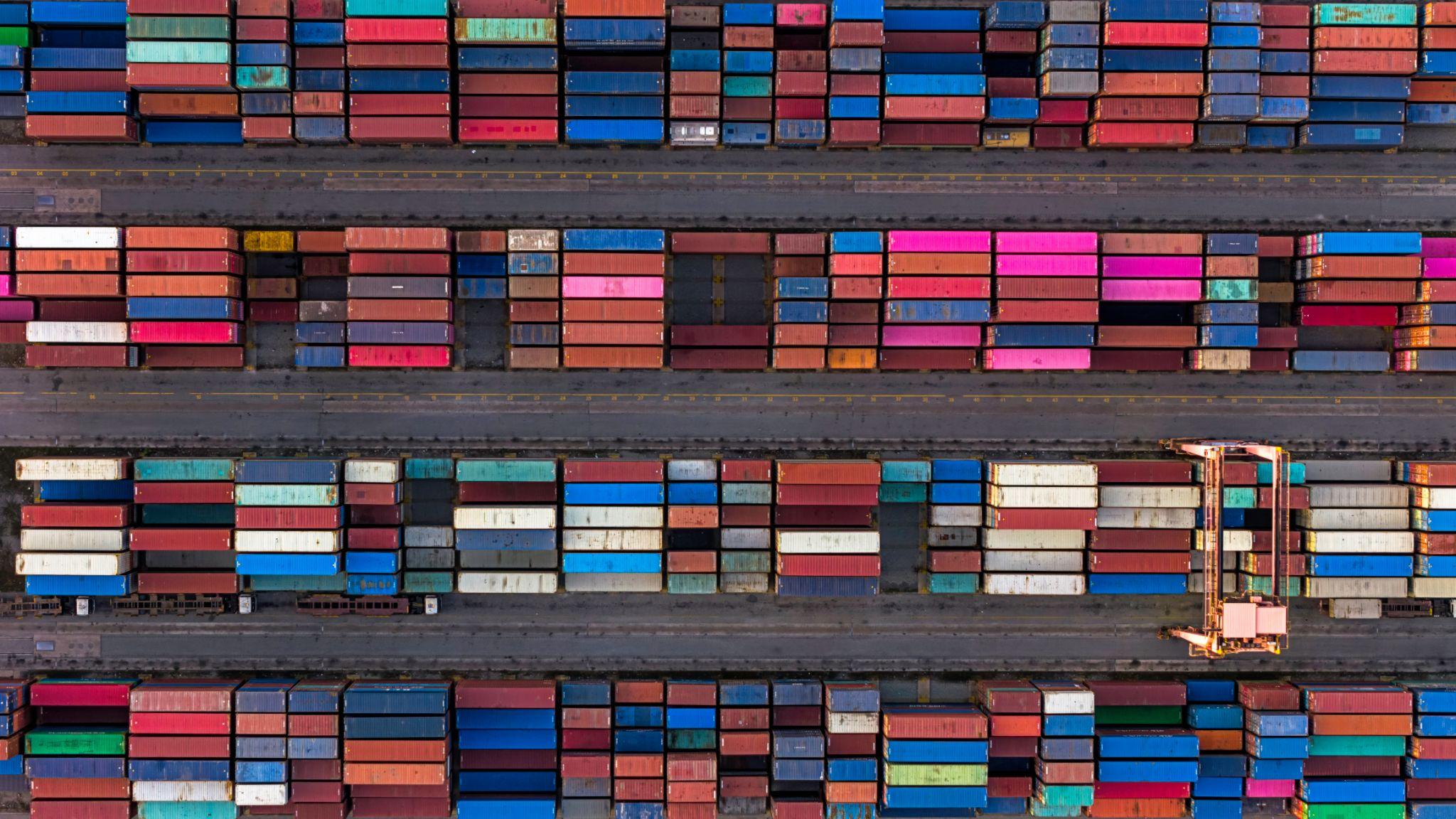 Aerial view of colorful shipping containers neatly stacked in rows at a large shipping yard.