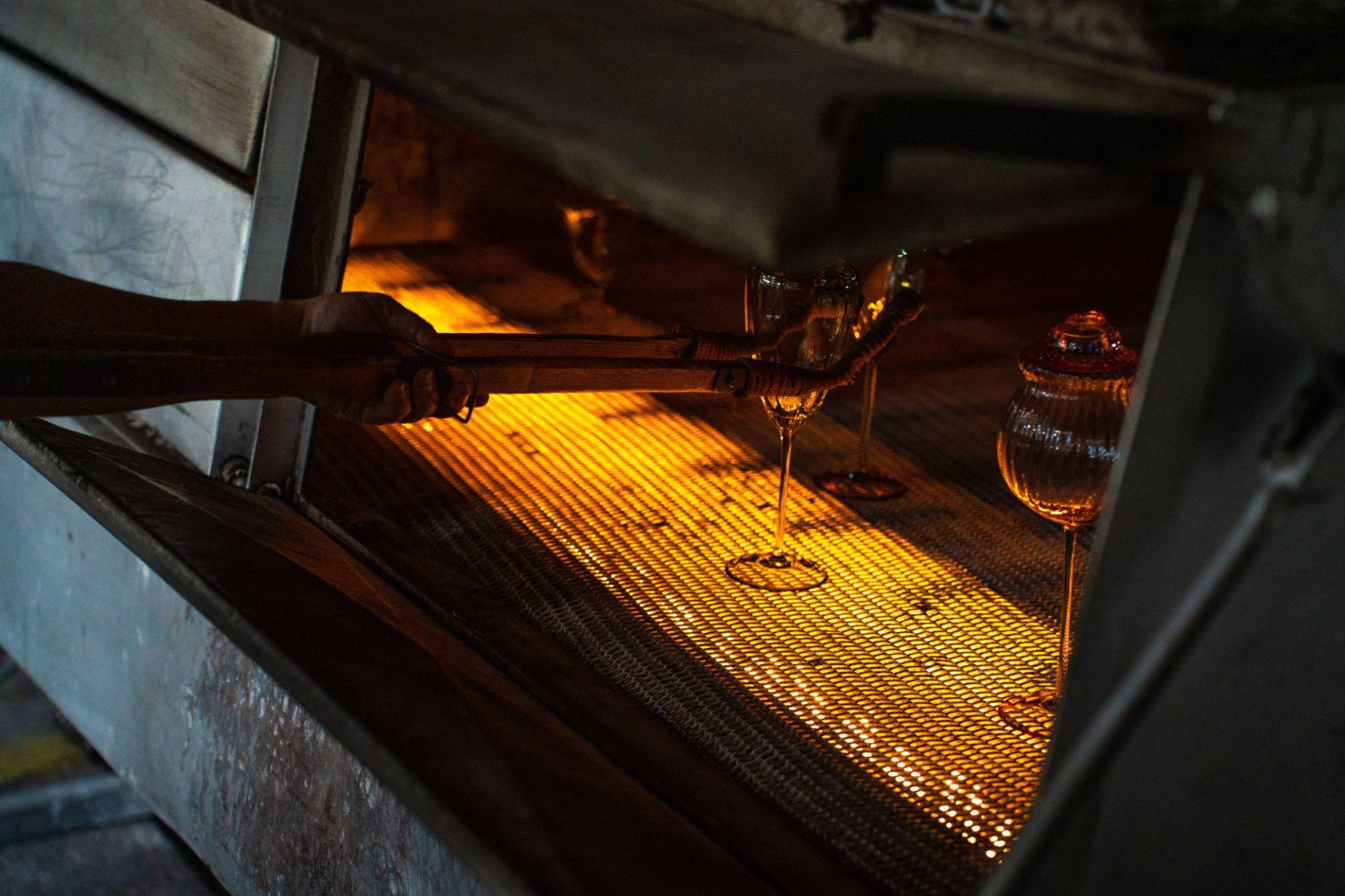Hand using tools to place glassware inside an oven with glowing heated mesh surface.
