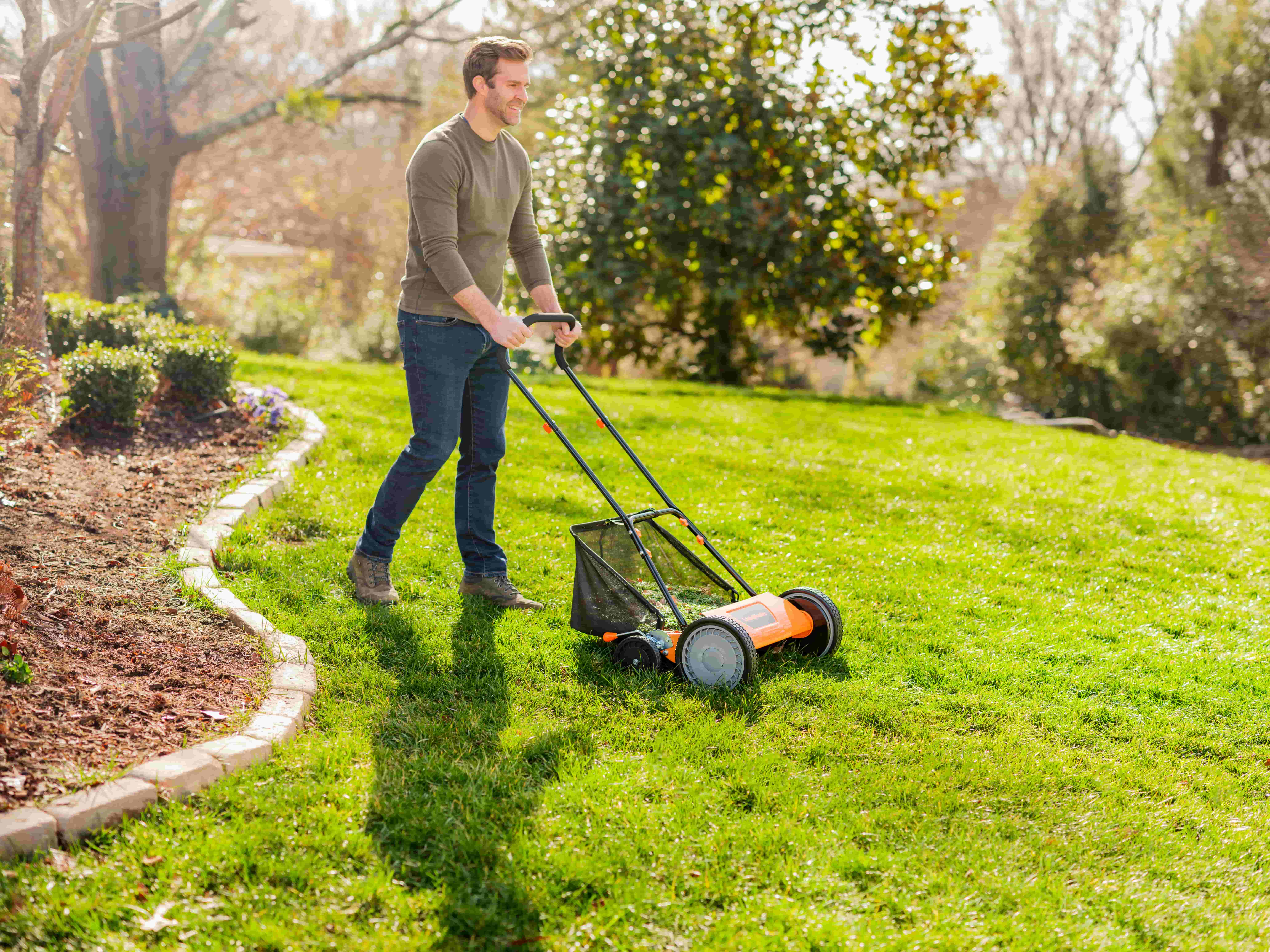 Man mowing a green lawn with a manual push lawn mower on a sunny day.