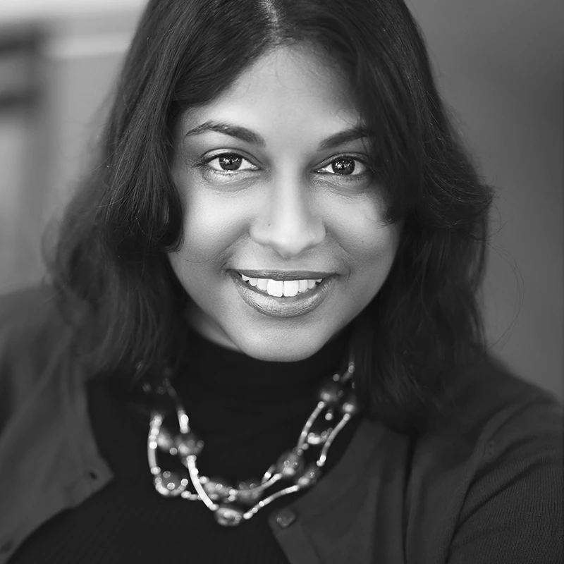 Smiling woman with medium-length dark hair wearing a dark top and a chunky beaded necklace.