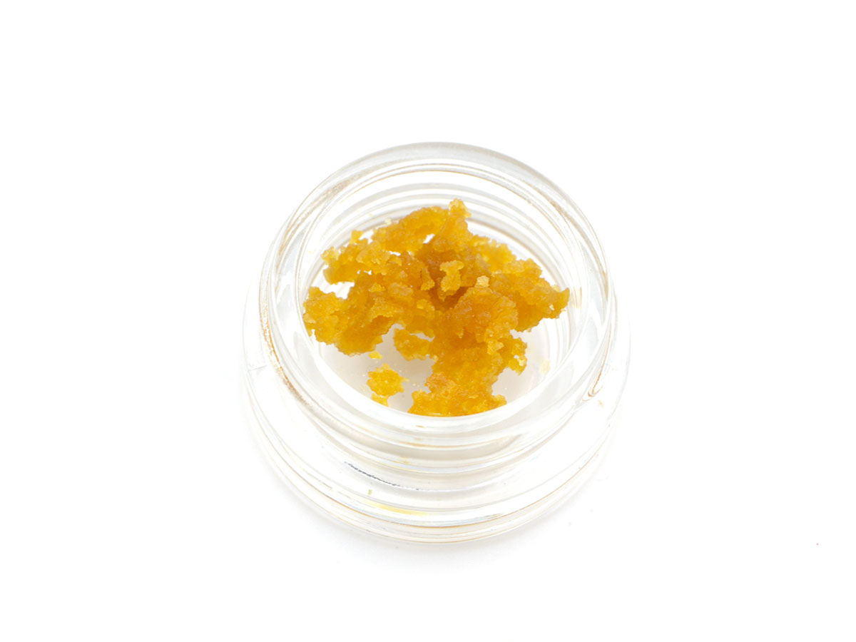 A small glass jar containing cannabis wax sits against a white background.