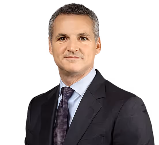 Middle-aged man with short gray hair wearing a dark suit, light blue shirt, and dark tie, facing forward with a neutral expression.