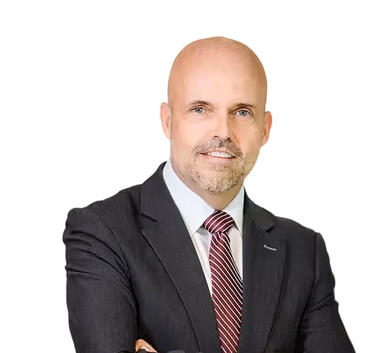 Bald man in a black suit with a white shirt and striped red tie, smiling with arms crossed.