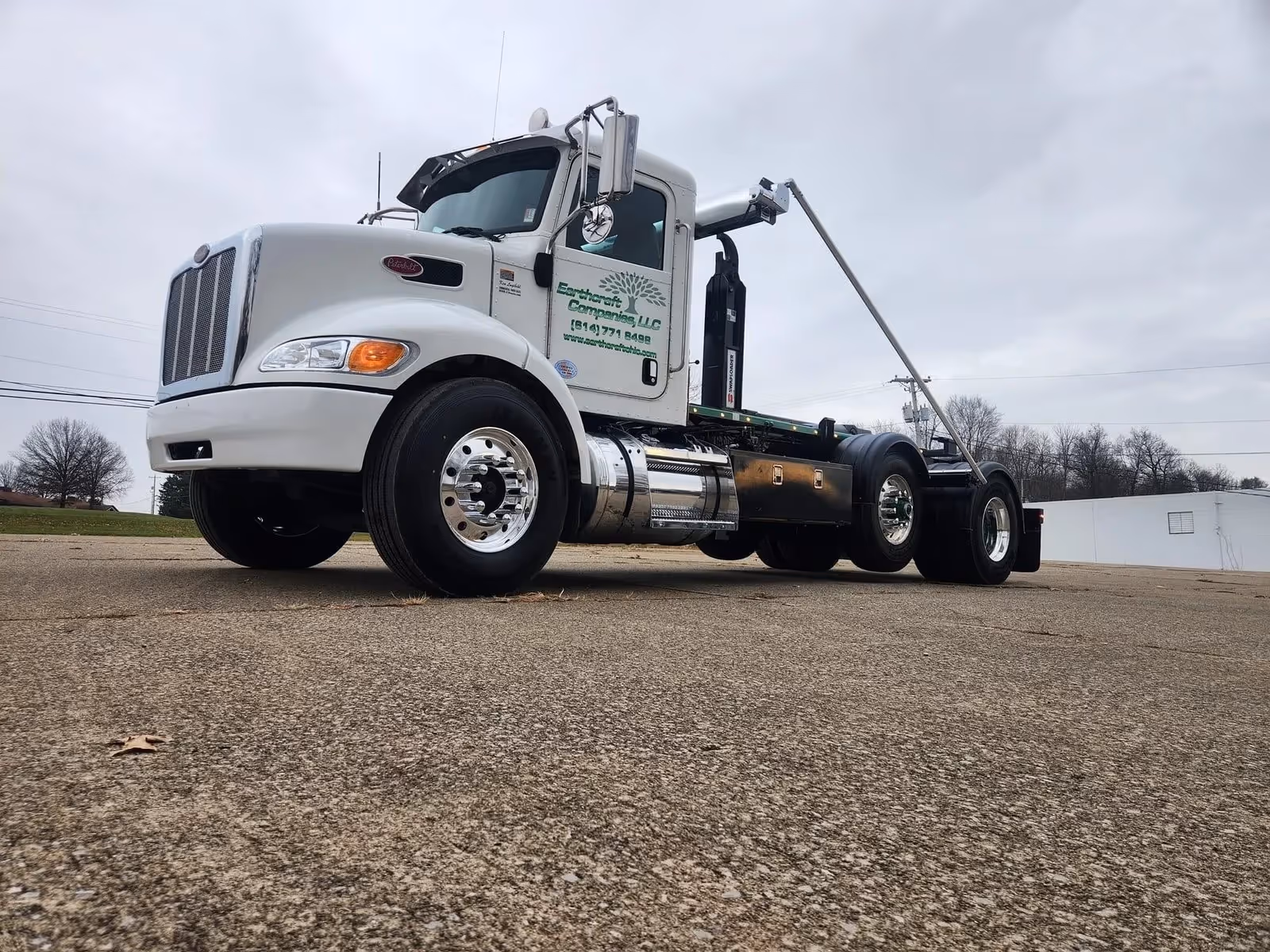 White Peterbilt roll-off truck with Earthcraft Companies LLC logo, parked on concrete under cloudy sky.