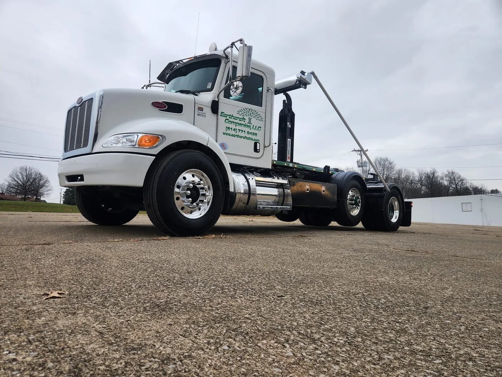White Peterbilt roll-off truck with Earthcraft Companies LLC logo, parked on concrete under cloudy sky.
