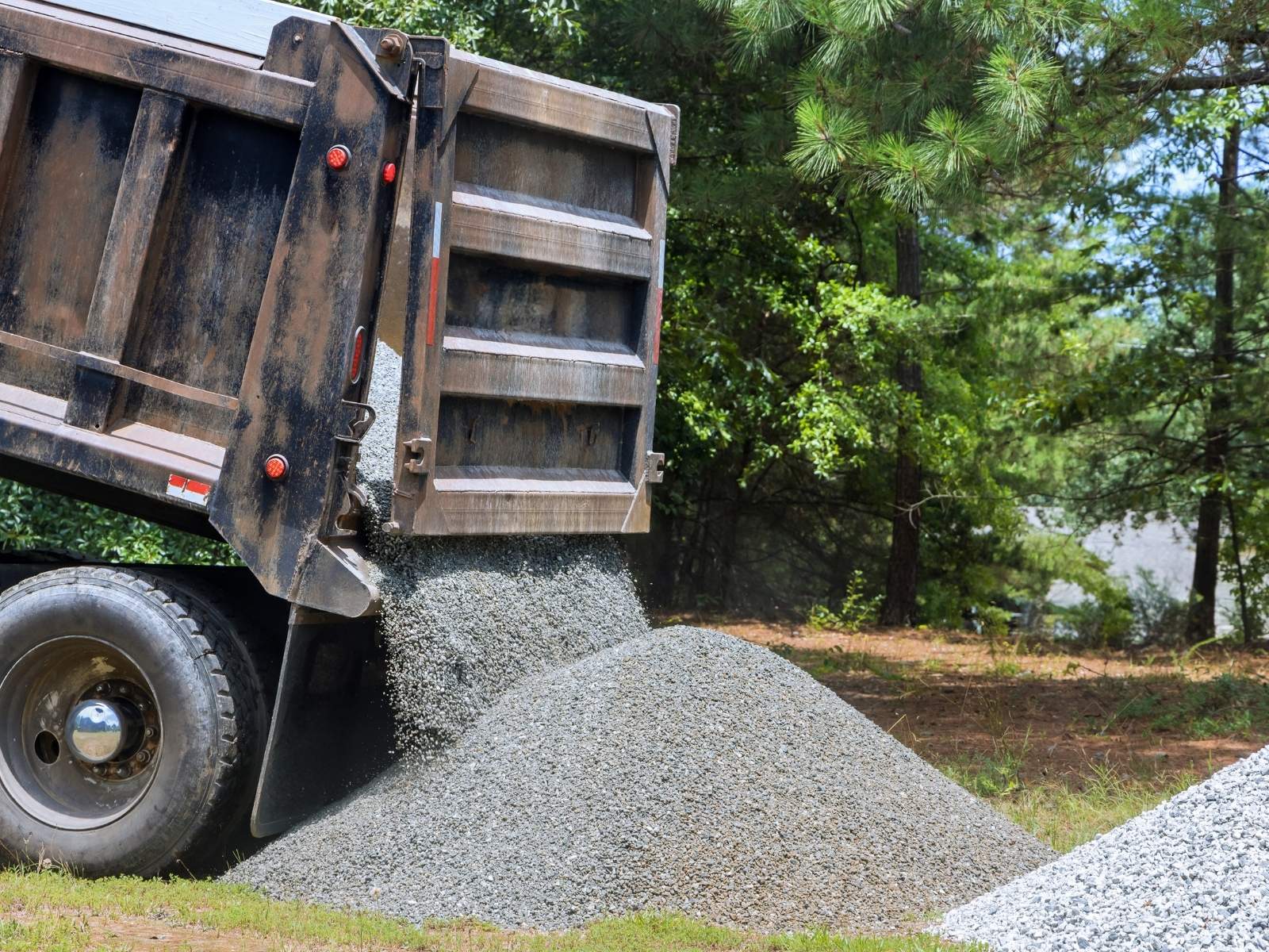 Dump truck unloading a pile of gravel in a forested outdoor area.
