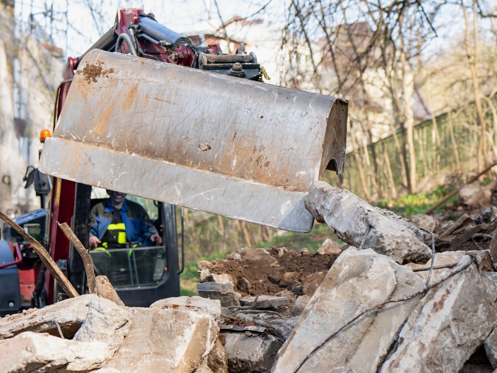 Excavator bucket lifting and moving broken concrete rubble at a demolition site with operator visible in the cabin.