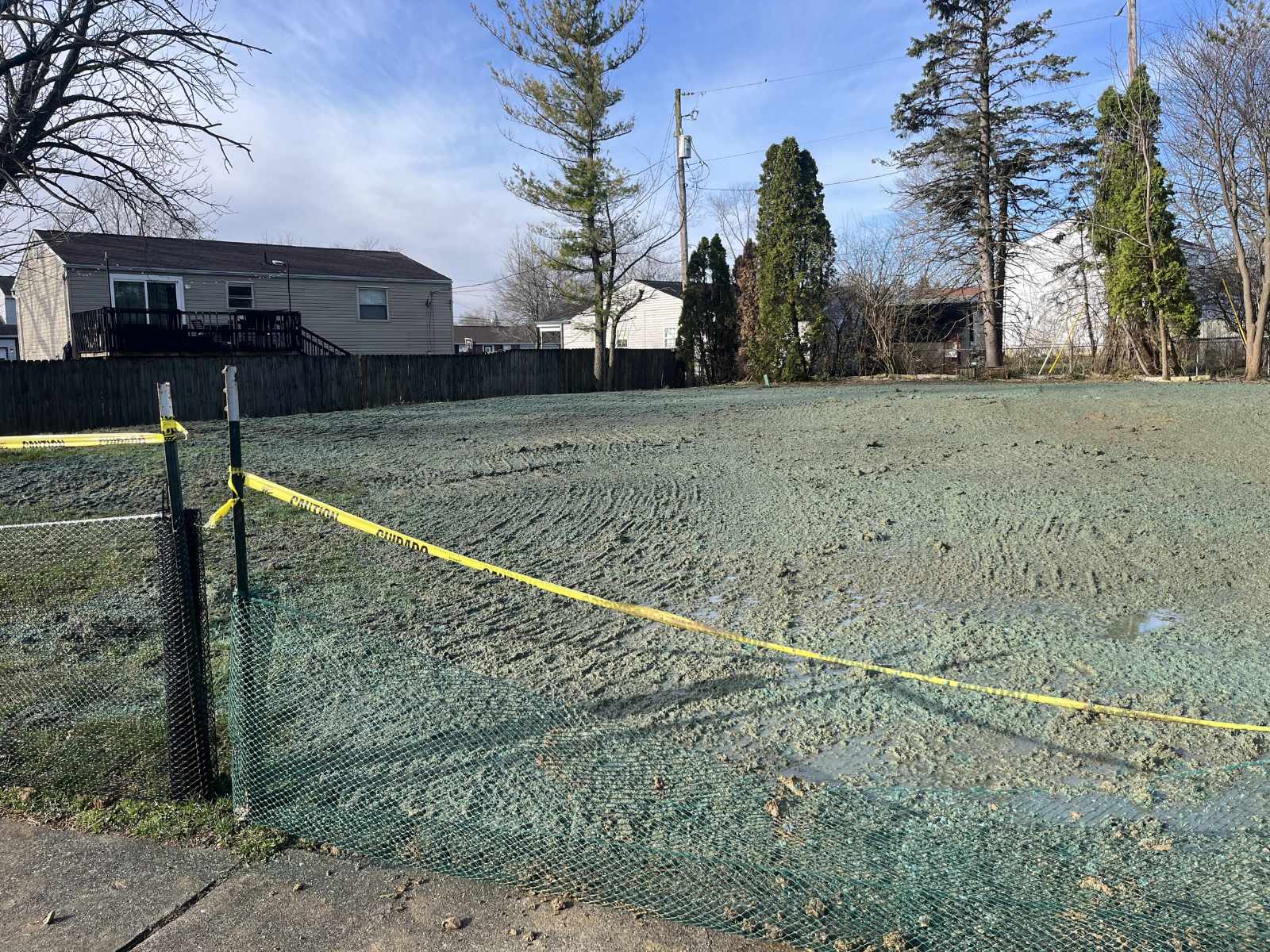 Open plot of land with freshly applied green hydroseeding material, surrounded by yellow caution tape and green mesh fencing.
