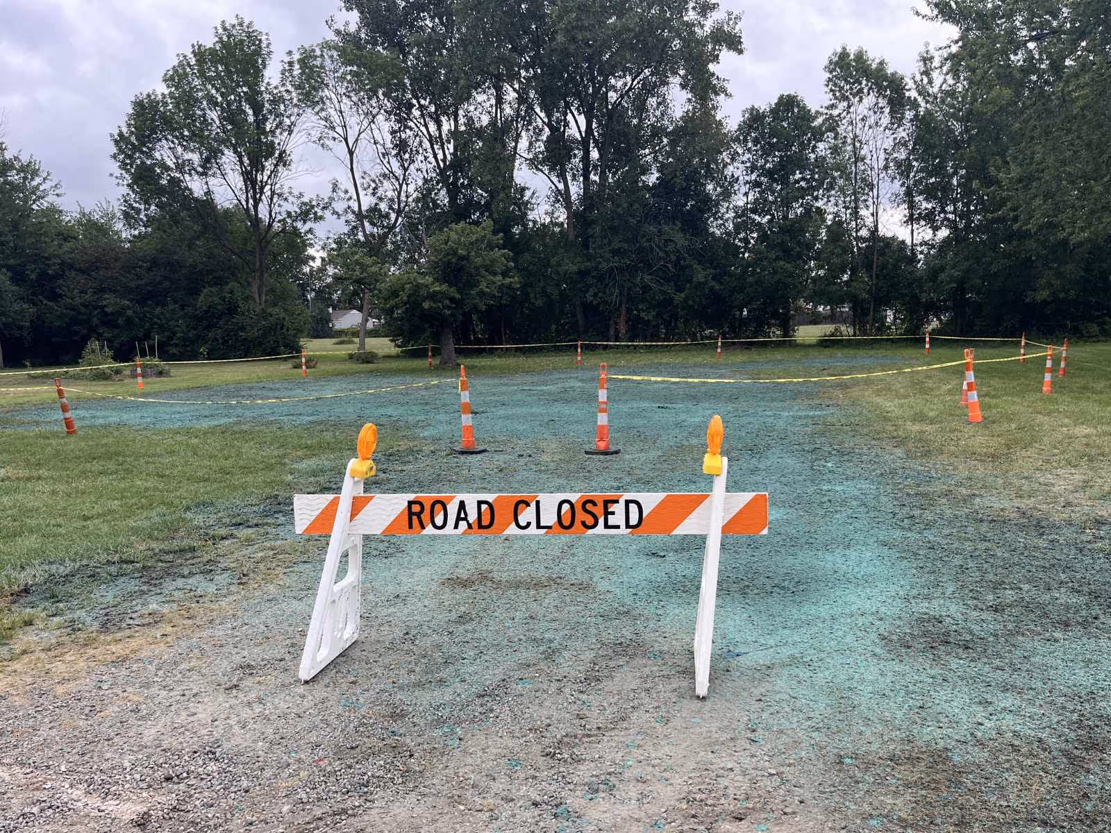 Construction area with orange and white 'ROAD CLOSED' barricade and cones around hydroseeded grass.