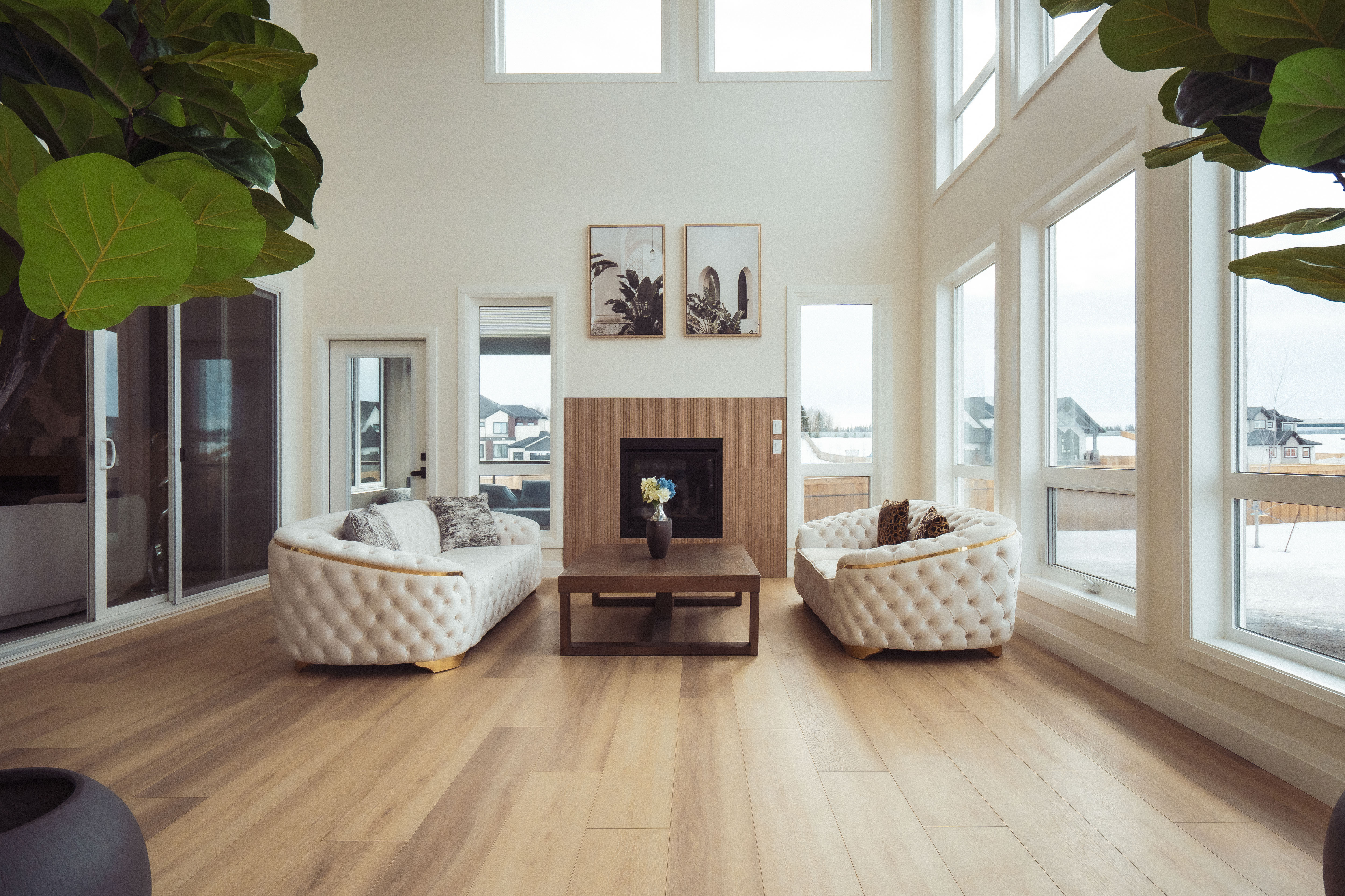 आधुनिक लिभिङ्ग रूममा दुई सेतो सोफा, बीचमा काठको टेबुल र भित्तामा फेमेल लगाएको फायरप्लेस।