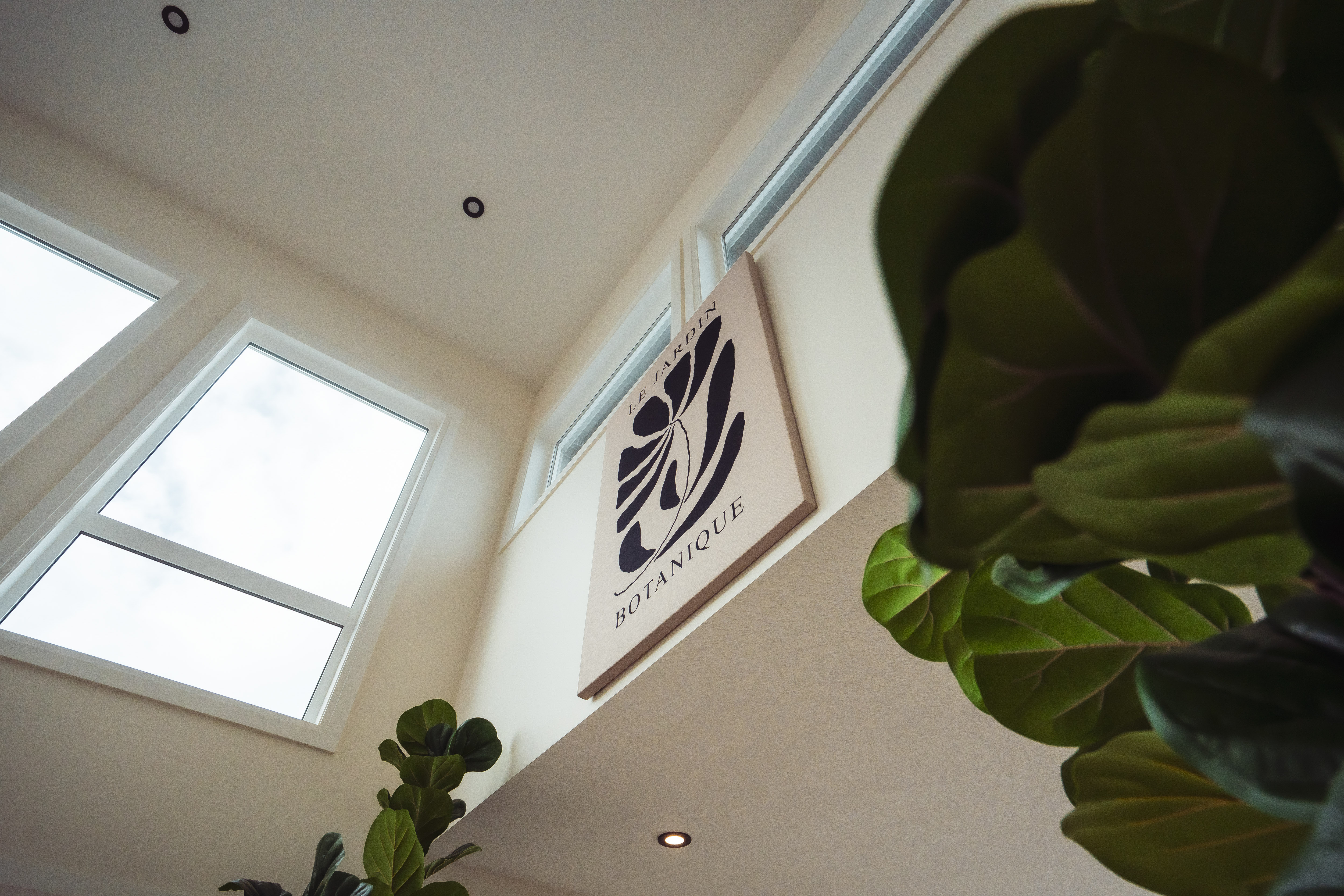 भित्तामा ठूलो झुण्डिएको पौधा चित्र सहित 'Le Jardin Botanique' लेखिएको बोर्ड र वरिपरि हरिया पातहरु भएको भित्री कोठा।