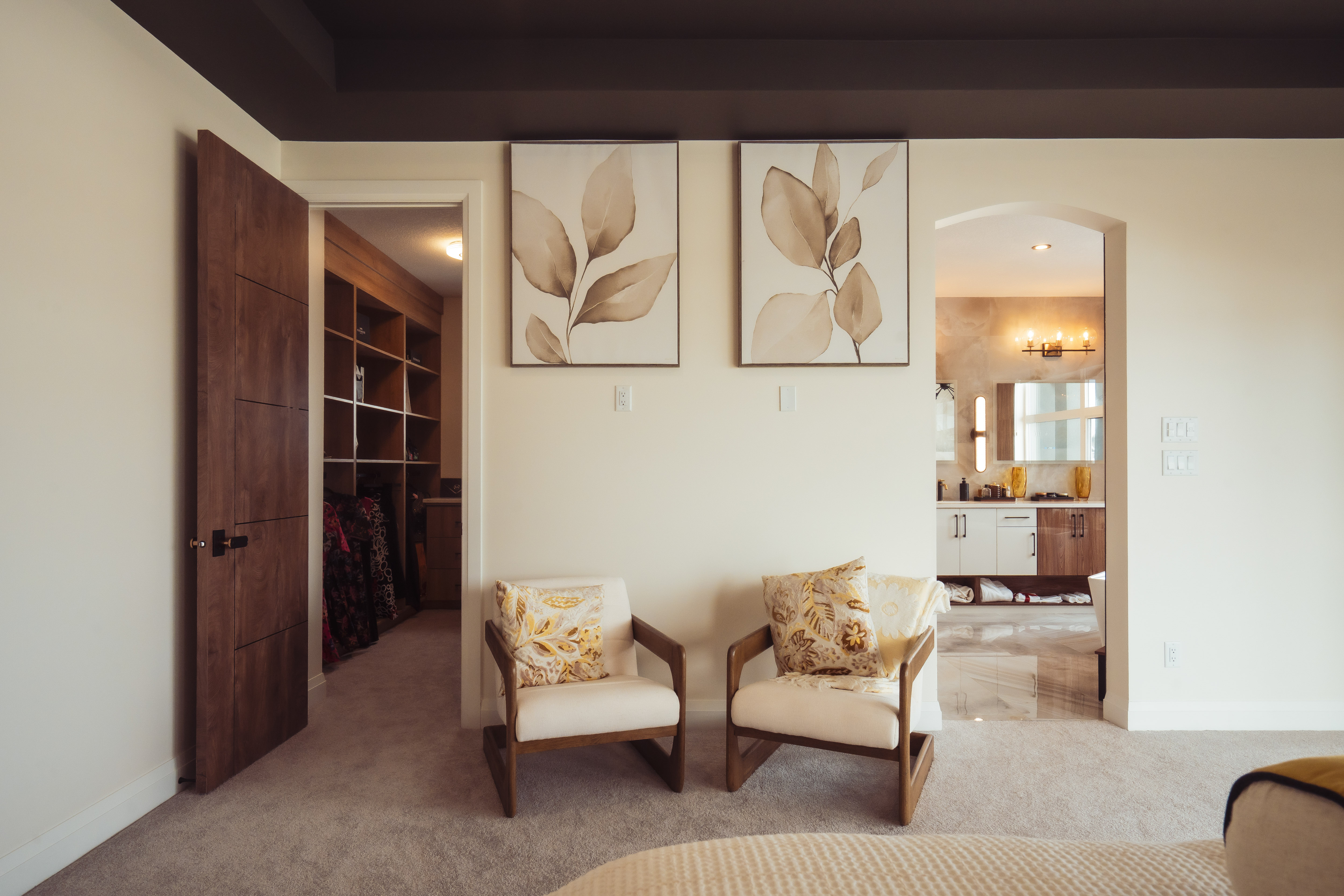 दुई काठको कुर्सीहरू सोफा कम्फ़र्टेबल बाक्लो कुशन र पातहरूको चित्र सहित पर्खालमा टाँसिएको। दायाँतिर खुल्ला ढोका र आरामकोठा।