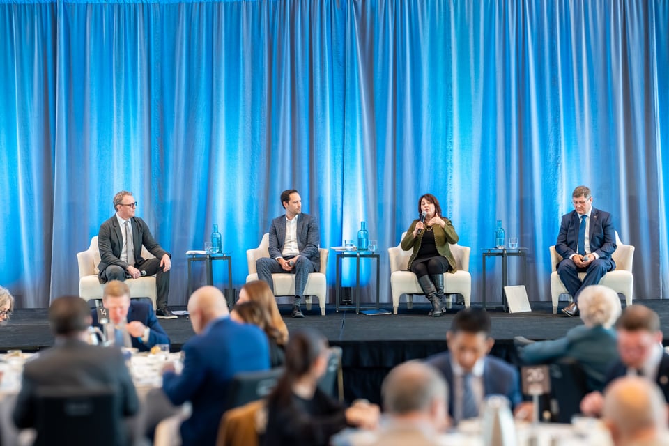 धेरै मानिसहरू खाना खाँदै गर्दा मंचमा चार जना, तीन जना पुरुष र एक महिला कुराकानी गर्दै।