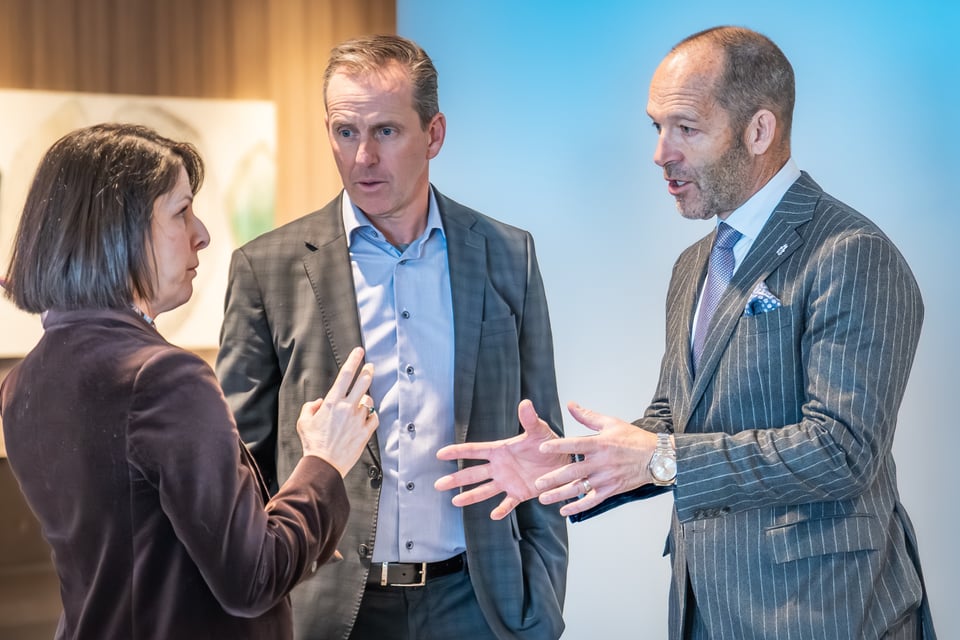 तीन व्यवसायीहरू औपचारिक पोशाकमा र कार्यालय वातावरणमा गम्भीर कुरा गर्दै।