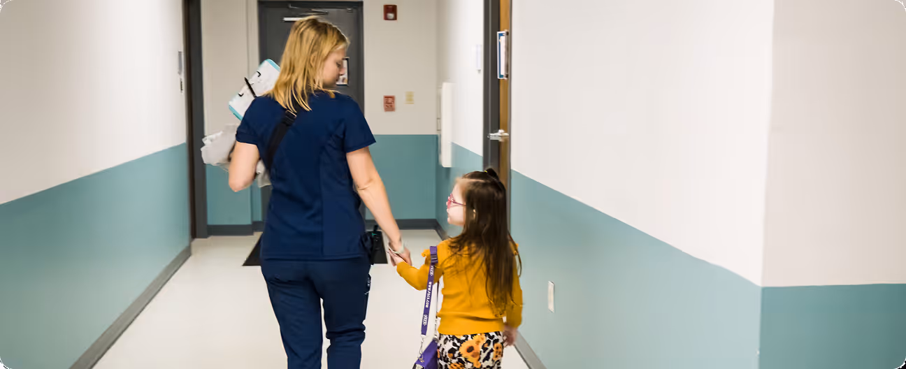 A BIG employee walking down a hallway holding hands with a child
