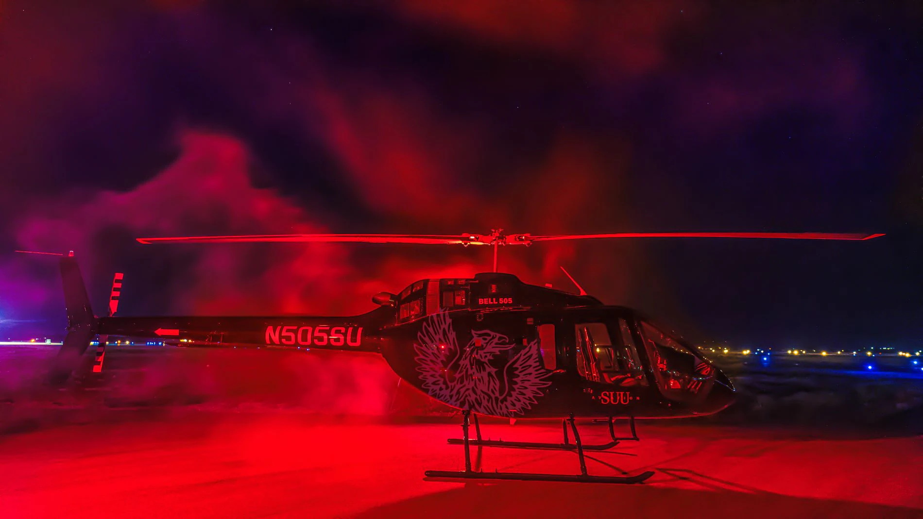 A black helicopter with red lights, featuring a stylized eagle design, on a dark runway.