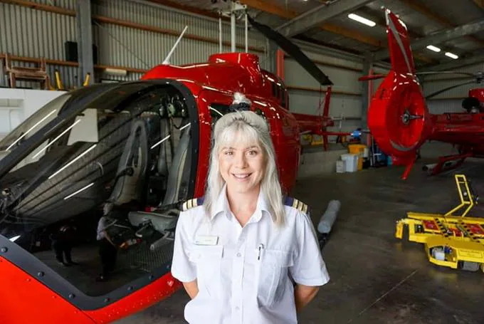 Female helicopter pilot smiling in front of a red helicopter in a hangar.