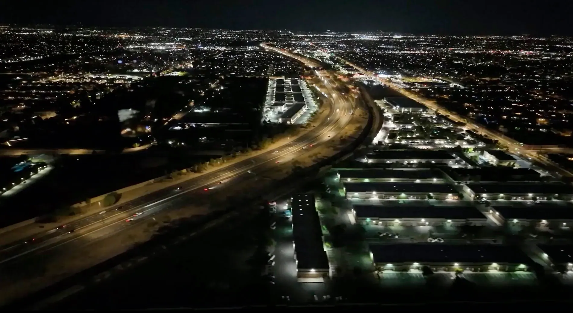 Night aerial view of a city with illuminated highways and buildings, showcasing urban lights.