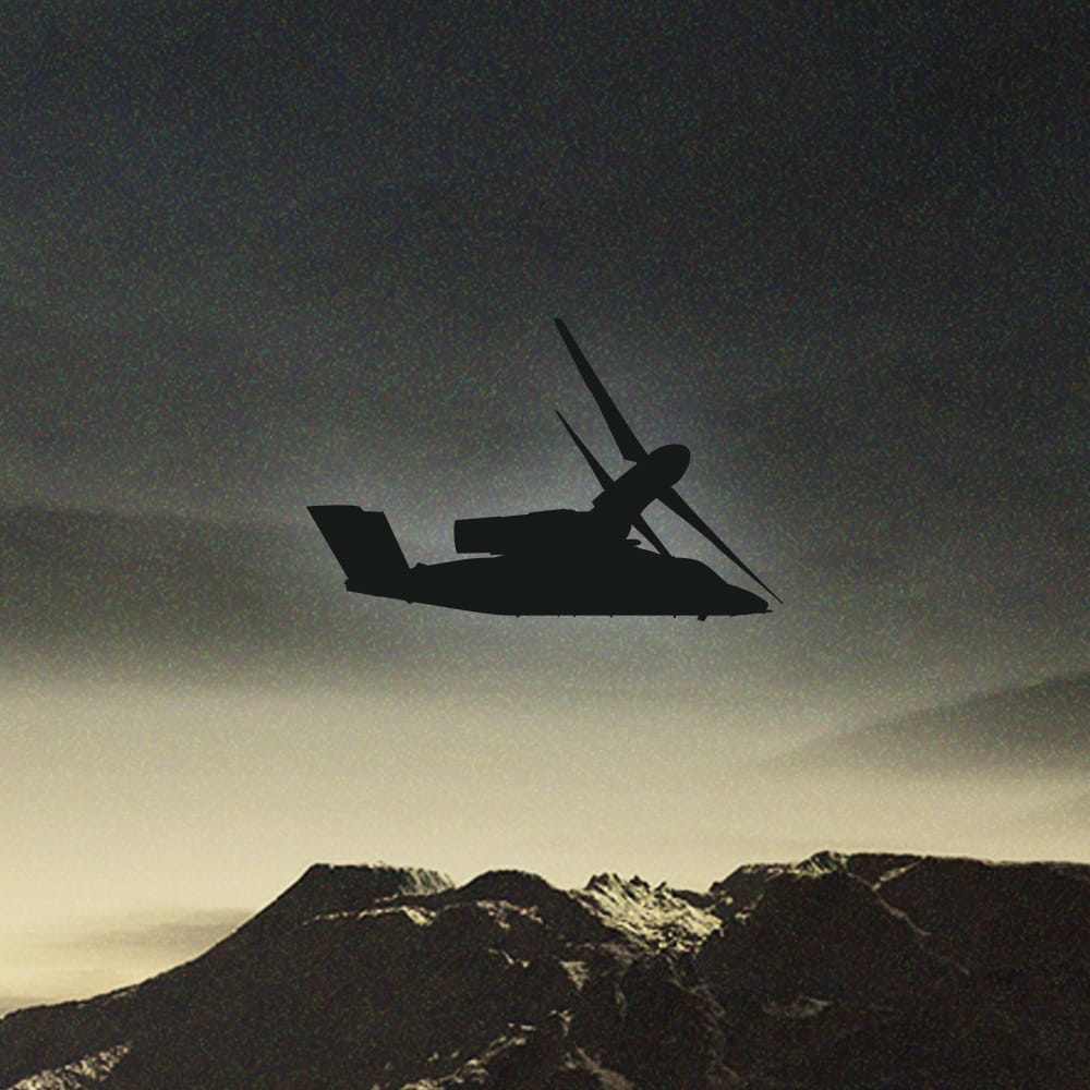 A silhouetted helicopter flying over a mountainous landscape at dusk.