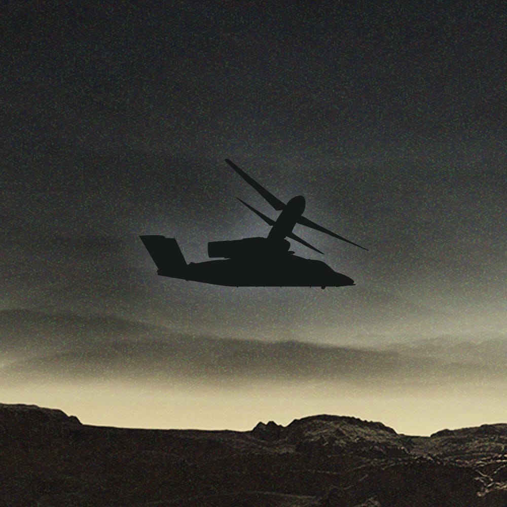 Silhouette of a helicopter flying against a dark, moody sky and mountainous landscape.