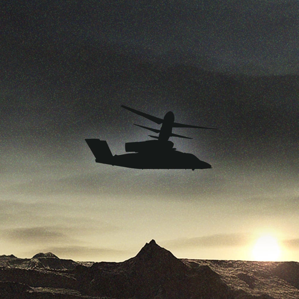 A silhouette of a helicopter flying over a mountainous landscape at sunset.