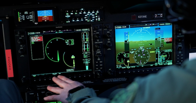Cockpit display screens showing flight data and navigation instruments with a hand on the controls.